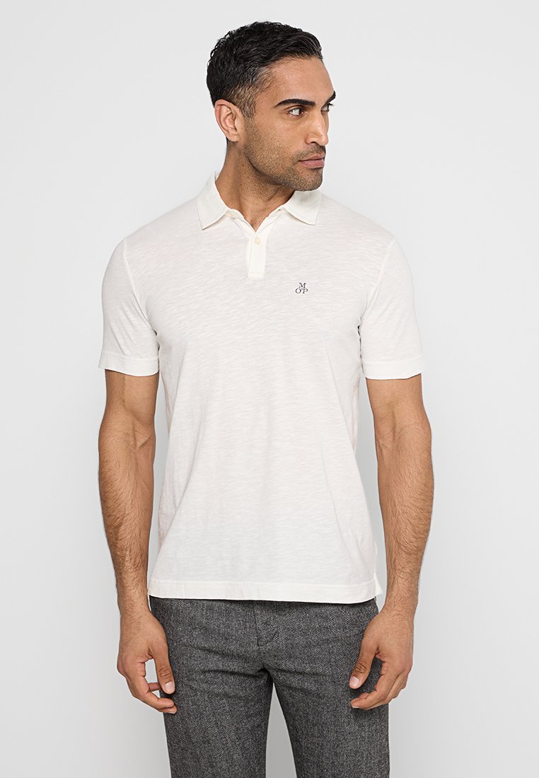 Helles beiges Polohemd aus weichem Stoff mit klassischem Kragen, kurzen Ärmeln und einem kleinen Logo auf der Brust, im entspannten Schnitt.