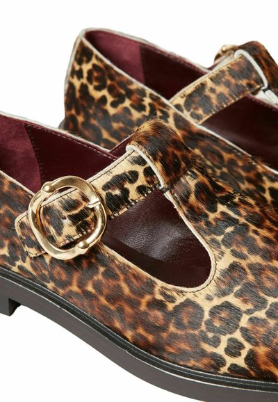 Chaussures plates à imprimé léopard en fausse fourrure avec une semelle noire épaisse, dotées d'un détail de sangle à boucle et d'une doublure intérieure bordeaux.