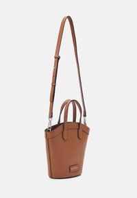 Sac à main en cuir marron avec des poignées courtes et une longue bandoulière réglable sur fond blanc.