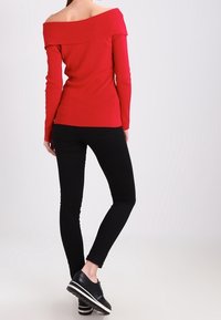 Top rosso scollato, design aderente, maniche lunghe, abbinato a jeans skinny neri e scarpe nere con dettagli bianchi. Texture liscia.