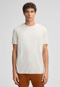 Helles Beige, Kurzarm-T-Shirt aus einem weichen, glatten Stoff. Rundhalsausschnitt und lockere Passform, kombiniert mit braunen Shorts.