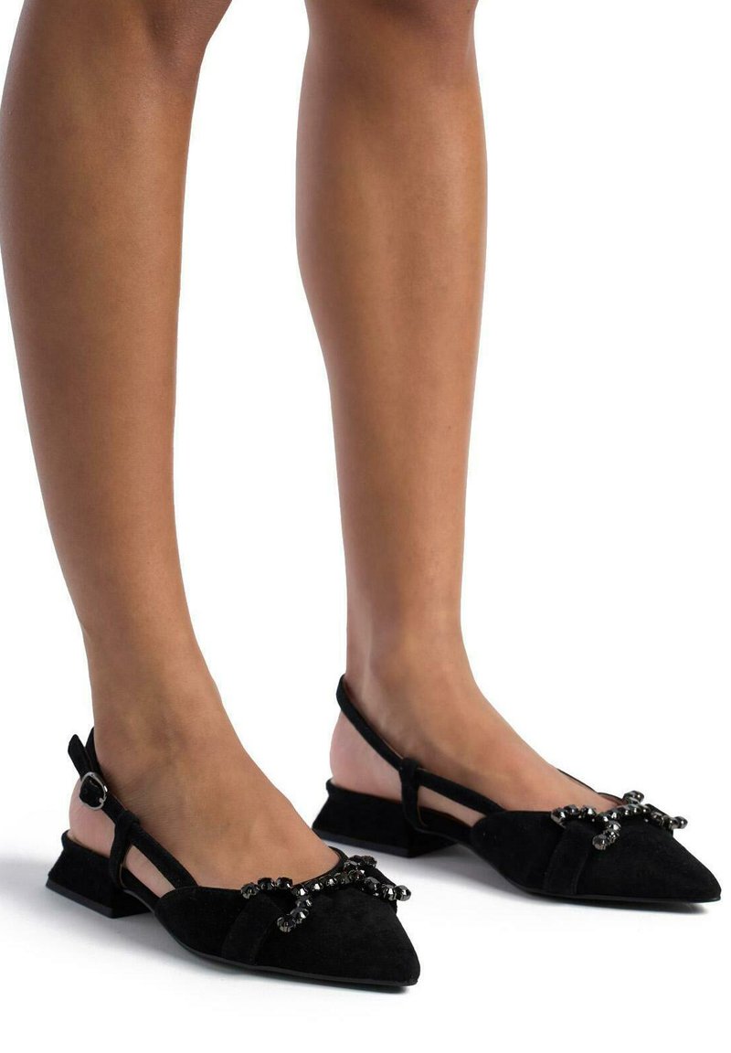 Bailarinas negras de ante con un diseño de punta y un bajo tacón cuadrado. Presentan adornos de cuentas en la parte delantera y una correa ajustable.
