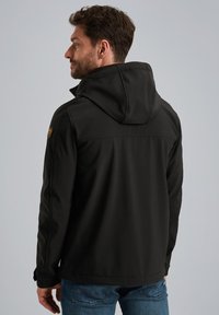 Zwarte softshell jas met capuchon, ritssluiting en een zachte textuur. Inclusief een logo accent op de schouder en aansluitende manchetten.