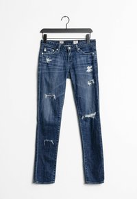 Úzké džíny v tmavě modrém denimu s opotřebovanými záplatami a třepenými okraji. Mají pět kapes a standardní pás s knoflíkovým zapínáním.