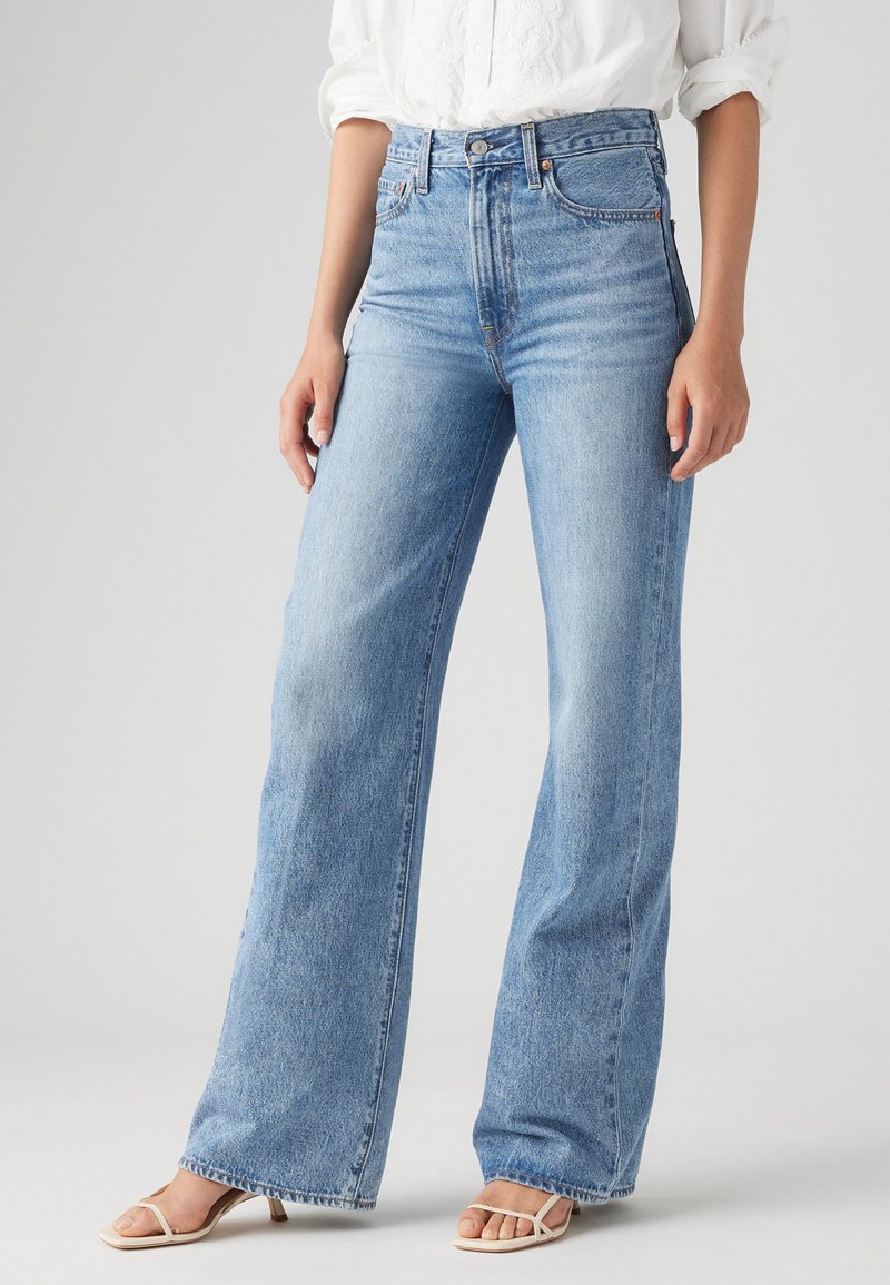 Jeans large taille haute de couleur bleu clair en denim ; avec une coupe droite, un design à cinq poches et un léger effet délavé pour un look vintage.