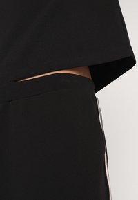 Svart atletisk tvådelad outfit med en croppad topp och högmidjade byxor med sidostrikar och en slät textur.