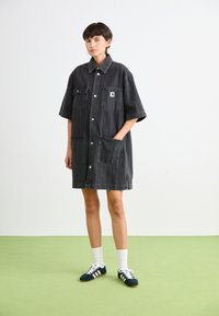 Schwarzes Jeanshemdkleid mit kurzen Ärmeln, ausgestattet mit zwei großen Fronttaschen, Knopfverschluss und einem kleinen Logo-Patch auf der Brust.