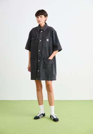 Black denim shirt dress with short sleeves, featuring two large front pockets, button closure, and a small logo patch on the chest.