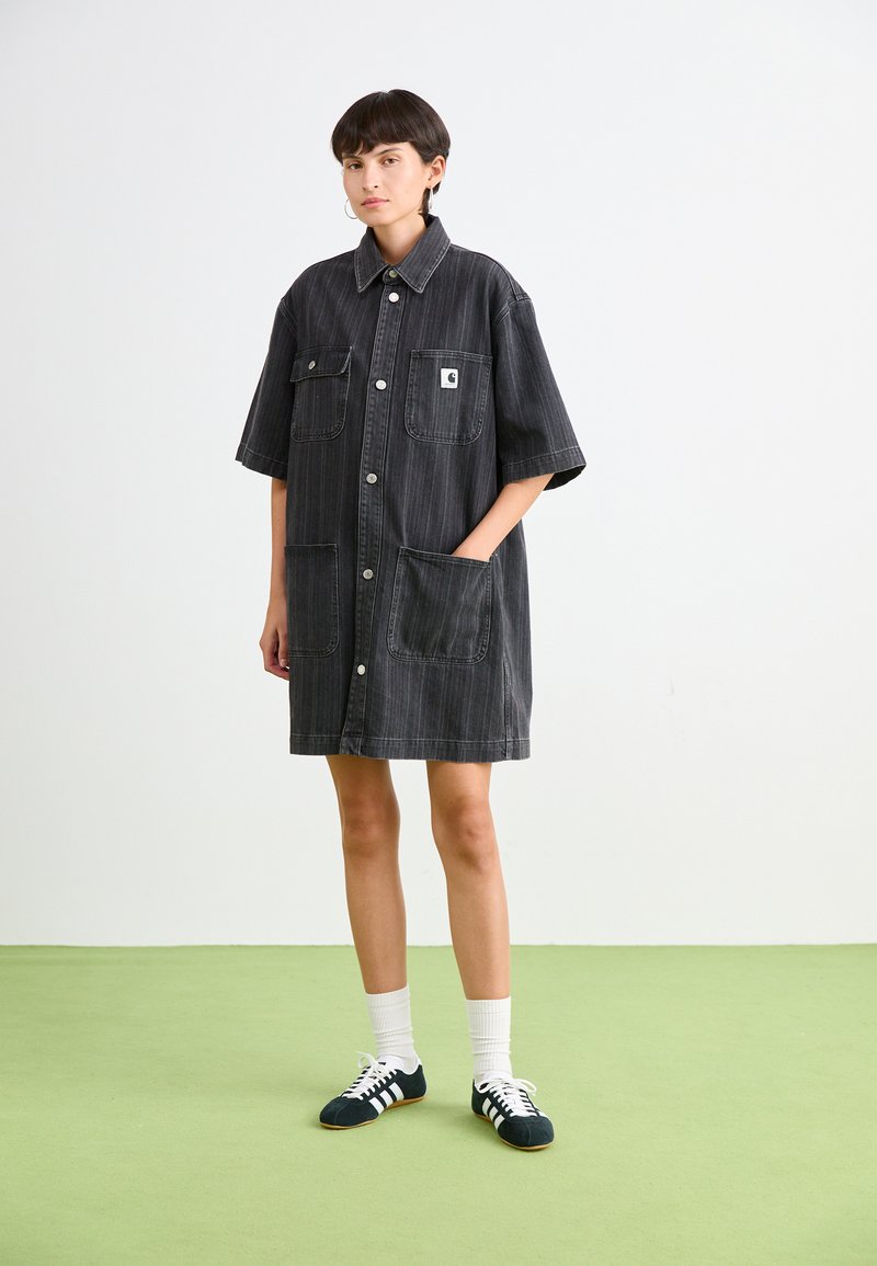 Schwarzes Jeanshemdkleid mit kurzen Ärmeln, ausgestattet mit zwei großen Fronttaschen, Knopfverschluss und einem kleinen Logo-Patch auf der Brust.