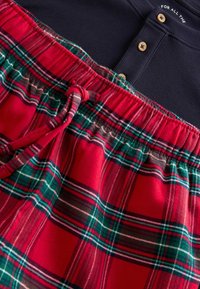 Rote karierte Schlafanzughosen mit einem grünen und weißen Muster, ausgestattet mit einem elastischen Bund und einem navyblauen Rippoberteil mit Holzknöpfen.