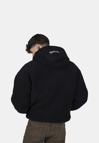 Felpa nera in pile con superficie testurizzata e cappuccio, con lettering ricamato bianco sul retro, design corto e vestibilità ampia.