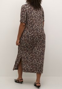 Femme portant une robe midi imprimé léopard avec fente sur le côté et manches courtes, associée à des escarpins noirs à talons bas et bride arrière, vue de dos.