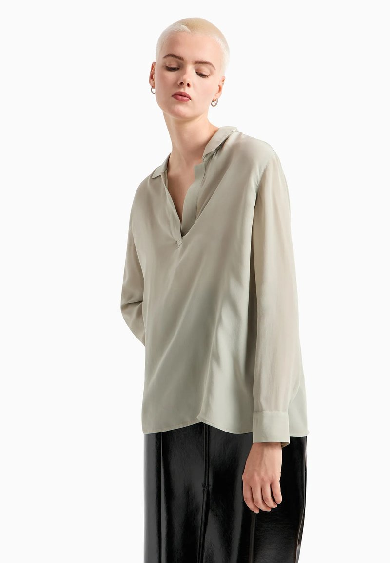 Blusa verde chiaro in tessuto setoso, con scollatura a V, maniche lunghe e orlo asimmetrico, abbinata a una gonna nera lucida.