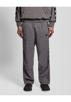 Donkergrijze casual broek voor heren met elastische taille, zijzakken, zwart vogel logo op de linker dij, gecombineerd met zwarte sneakers.