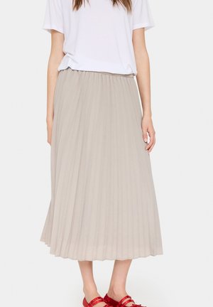 Pleated, knee-length beige skirt made of lightweight fabric, featuring an elastic waistband and paired with red sandals.
