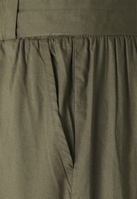 Tissu vert olive avec des coutures froncées et une poche latérale sur un vêtement.