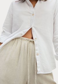 Witte linnen shirt met kraag, knoopsluiting aan de voorkant en een ontspannen pasvorm, gecombineerd met lichtbeige linnen broek met een trekkoord in de taille.