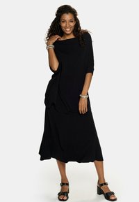 Czarna sukienka z miękkiego materiału, o luźnym kroju, z krótkimi rękawami i długości do kostek. Noszona z czarnymi sandałami i srebrnymi bransoletkami.