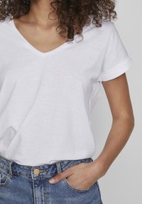 T-shirt blanc à col en V avec des manches courtes retroussées, fabriqué en tissu doux, associé à un jean en denim bleu taille haute. Coupe décontractée.
