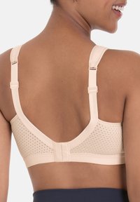 Beige bra with a breathable mesh back, wide straps, and adjustable hardware. Features a smooth texture and a rounded shape.