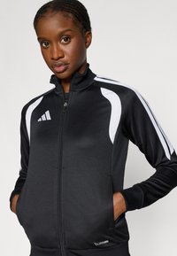 Μαύρο ζακέτα με φερμουάρ, με λευκές λεπτομέρειες, υψηλό γιακά, πλαϊνές τσέπες και αεριζόμενο ύφασμα με την ένδειξη "CLIMACOOL".