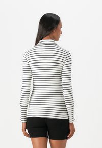 Långärmad, figursydd topp med ribbad textur, prydd med vertikala svart-vita ränder. Kragen är platt och designen är ogenomskinlig.