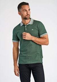 Camisa polo verde con cuello gris y acentos a rayas, fabricada con una tela texturizada, que cuenta con un cierre de tres botones y un detalle de logo.