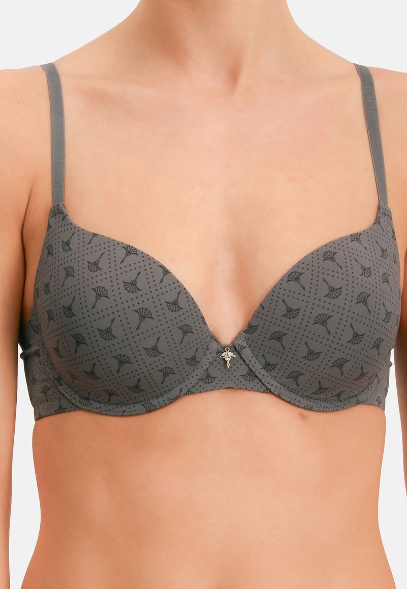 Sujetador gris con aros y patrón floral negro, con tirantes ajustables, usado en el torso superior y los hombros de una persona.