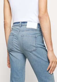 Vaqueros de denim de un azul claro con forma ajustada, con bolsillos traseros y una etiqueta blanca en la cintura. Tejido texturizado.