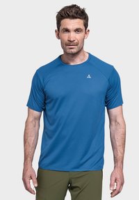 Blaues kurzärmliges Sportshirt aus strukturiertem Stoff, mit Rundhalsausschnitt und kleinem Logo. Kombiniert mit olivgrünen Hosen.