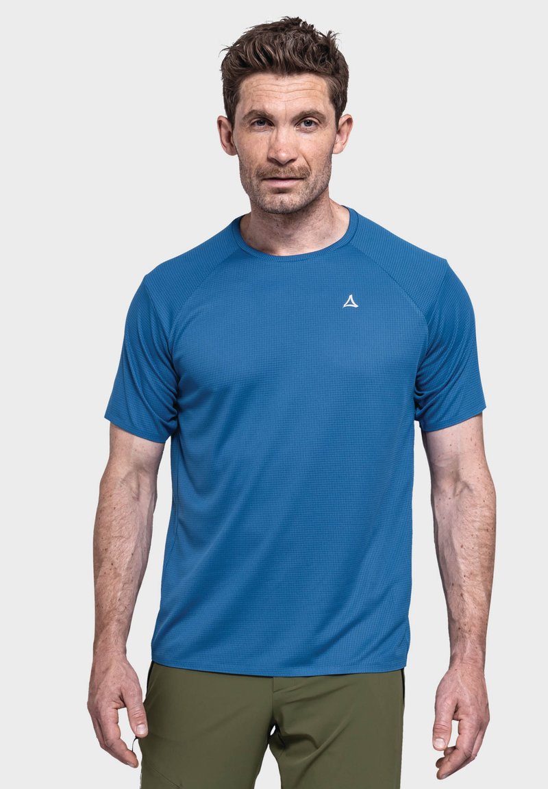 Blaues kurzärmliges Sportshirt aus strukturiertem Stoff, mit Rundhalsausschnitt und kleinem Logo. Kombiniert mit olivgrünen Hosen.