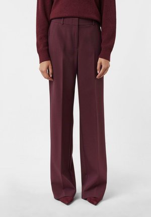 Woman wearing high-waisted, wide-leg burgundy trousers paired with a matching burgundy sweater and pointed shoes.