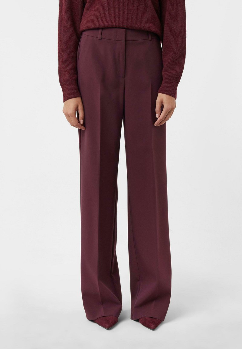 Woman wearing high-waisted, wide-leg burgundy trousers paired with a matching burgundy sweater and pointed shoes.