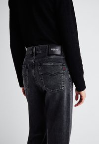 Black denim jeans with a high waist, featuring a black logo tag on the back, subtle fading, and classic five-pocket design.