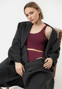 Ciemnoszary wełniany płaszcz noszony rozpięty na bordowym topie typu tank i dopasowanych bokserkach, charakteryzujący się gładką fakturą, luźnym krojem i minimalistycznym designem.