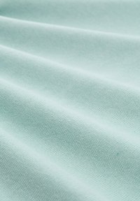 Hell mintgrüner Stoff mit einer glatten, strukturierten Oberfläche und sichtbaren Falten, hergestellt aus einem gewebten Material, das eine weiche Oberfläche zeigt.