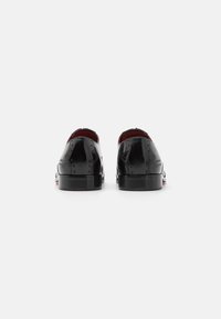 Scarpe in vernice nera con una finitura liscia, punta arrotondata e tacco basso. Presentano sottili motivi a diamante e un interno rosso.