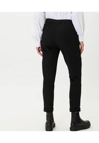 Pantalones negros de cintura elástica con un ajuste tapered, que cuentan con bolsillos laterales y puños enrollados. Tejido texturizado que se ve con botas negras hasta el tobillo.
