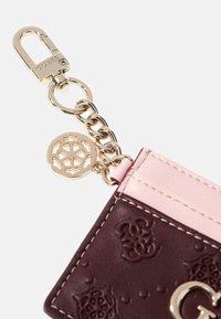 Porte-cartes en cuir de couleur bourgogne foncé avec des accents roses, des détails texturés, des éléments en or et un charm décoratif en forme de flocon de neige.