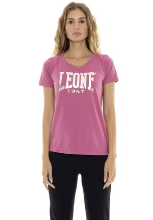 Une femme porte un T-shirt Leone 1947 rose à manches courtes et un pantalon noir sur fond blanc.