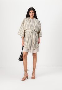 Prúžkovaný kimono župan v béžovej a zelenej farbe s otvoreným predným dielom, viazacím pásom a širokými rukávmi. Kombinované so svetlými šatami, čiernou taškou a sandálmi na opätku.