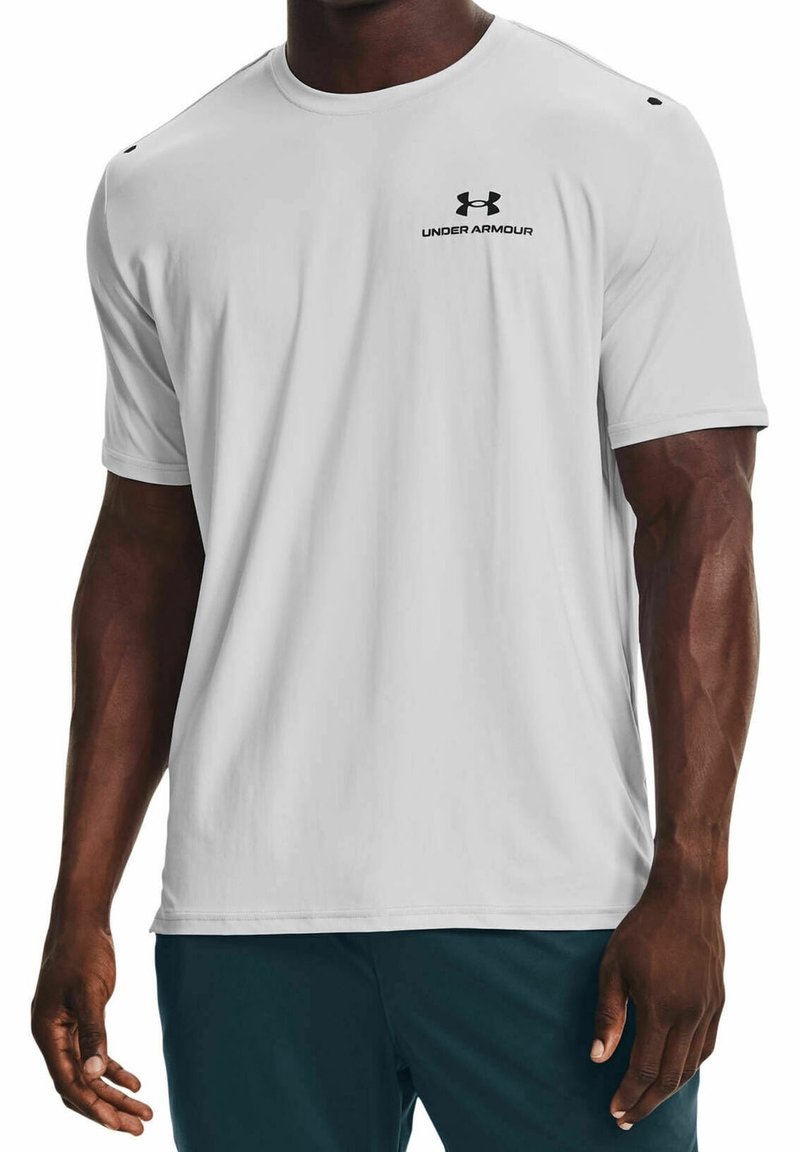 Homme portant un T-shirt Under Armour blanc uni à manches courtes et un short de sport foncé, debout avec les bras détendus le long du corps.