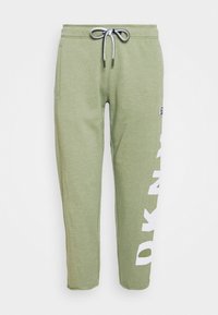 Ljusgröna joggare med vit dragsko och stor vit vertikal text på höger ben, framifrån och med sidofickor.