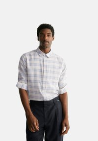 Camicia a maniche corte con bottoni, leggermente decorata, con colletto, caratterizzata da quadretti blu e lavanda su sfondo bianco. Pantaloni scuri.