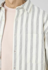 Chemise à rayures beige et marine, dotée d'une poche poitrine, d'une texture douce et d'un col classique. En dessous se trouve une chemise rose pâle.