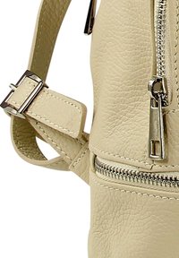 Sac en cuir texturé beige avec des fermetures éclair en argent et une boucle de sangle ajustable.