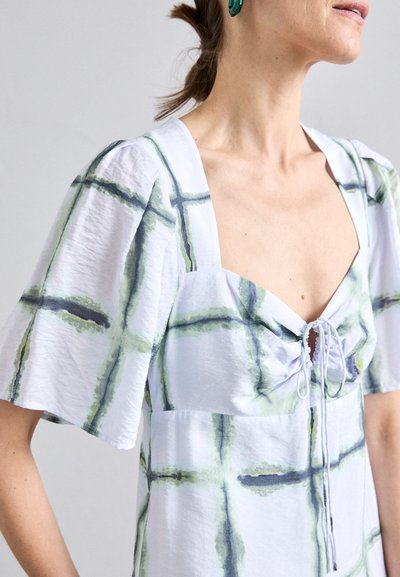 Witte jurk met groen en zwart ruitpatroon, korte puffmouwen, vierkante halslijn en trekkoorddetail aan de voorkant. Gladde textuur.