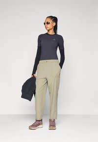 Crna dugodlaka, uska majica od teksturiranog materijala; svijetlozelene hlače širokog kroja; siva oversize jakna; smeđe tenisice s vezicama.