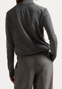 Grau gestrickter Pullover mit hohem Kragen, der eine glatte Textur und eine taillierte Passform aufweist, kombiniert mit maßgeschneiderten grauen Hosen mit Gesäßtaschen.