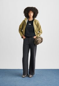 Olive green waterproof jacket, black t-shirt, dark grey wide-leg pants, and grey sneakers. Brown textured handbag with short handles.